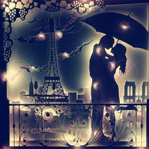 May include: A silhouette of a couple kissing under an umbrella in front of the Eiffel Tower. The couple is standing on a balcony with a wrought iron railing. The background is a cityscape with a cloudy sky.