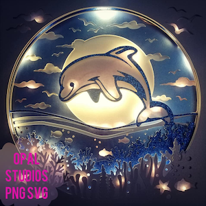 May include: A blue and gold nightlight with a dolphin jumping over a moon and coral reef. The nightlight is lit up and has a glittery finish.