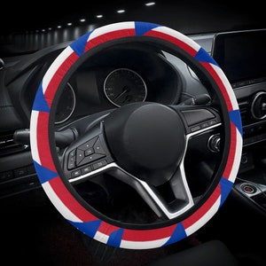 May include: A black steering wheel cover with a red, white, and blue pattern. The cover has a geometric design with stripes and squares.