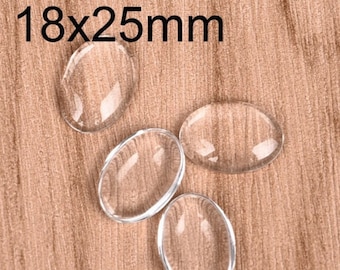 Pode incluir: Quatro cabochões ovais de vidro transparente, cada um medindo 18 mm por 25 mm, estão dispostos sobre uma superfície de madeira.