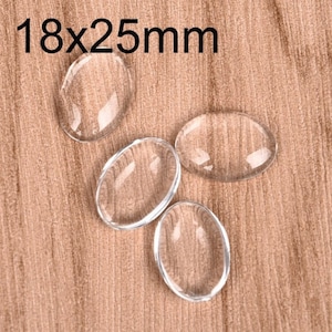 Puede incluir: Cuatro cabujones ovalados de vidrio transparente, cada uno mide 18 mm por 25 mm, están dispuestos sobre una superficie de madera.
