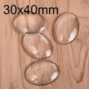 May include: Four clear glass cabochons, each measuring 30mm by 40mm, are arranged on a wooden surface.