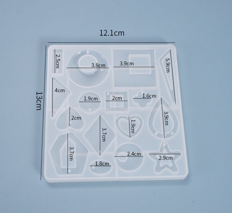 May include: A clear silicone mold with 13 different shapes for making jewelry. The mold measures 12.1 cm by 13 cm and includes shapes like a heart, star, circle, and square.