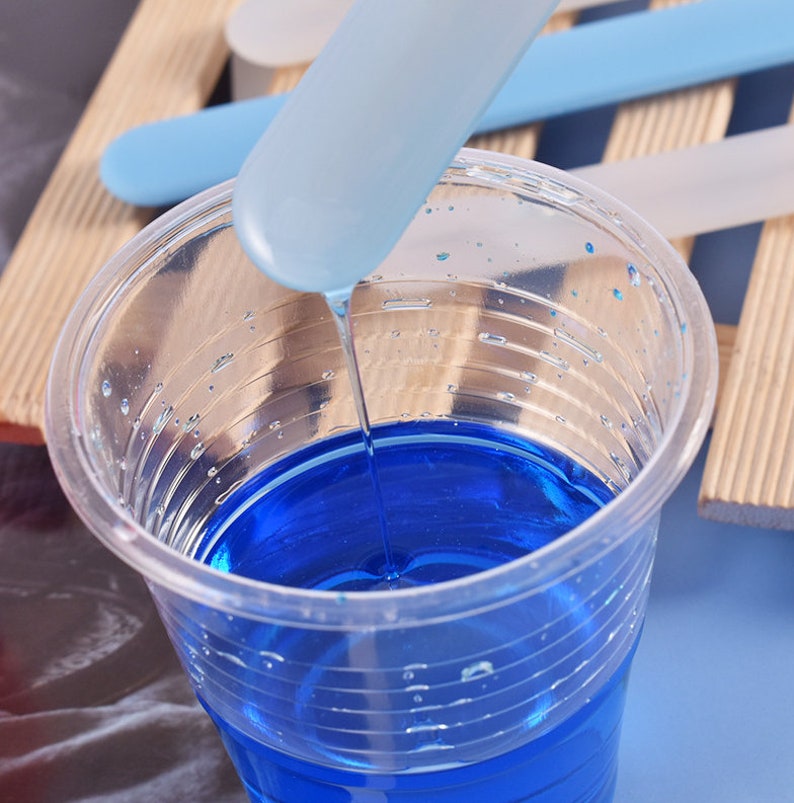 May include: A clear plastic cup filled with blue resin, with a blue plastic stirring stick dripping resin into the cup.