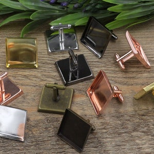 Puede incluir: Una colección de gemelos en varios acabados metálicos, incluyendo dorado, plateado, cobrizo y negro. Los gemelos presentan diseños cuadrados y en forma de diamante, con cierre de barra en T. Dispuestos sobre una superficie de madera.