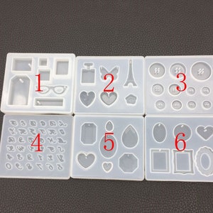 May include: Six white silicone molds for making resin jewelry. The molds are numbered 1 through 6 and contain various shapes, including hearts, tags, glasses, a perfume bottle, a butterfly, the Eiffel Tower, buttons, and a teardrop.