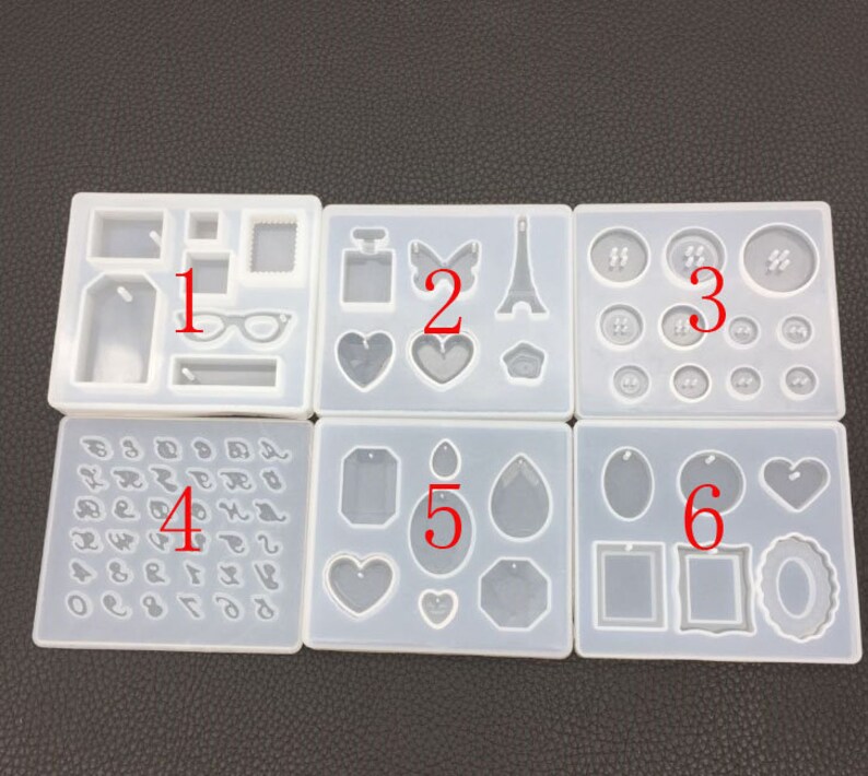 May include: Six white silicone molds for making resin jewelry. The molds are numbered 1 through 6 and contain various shapes, including hearts, tags, glasses, a perfume bottle, a butterfly, the Eiffel Tower, buttons, and a teardrop.