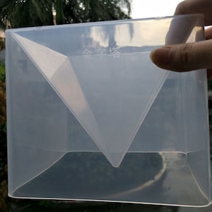May include: A clear plastic mould for making a triangular shaped cake. The mould has a smooth surface and is designed to create a three-dimensional cake with a pointed top. The mould is labelled "金字塔" which translates to "pyramid" in English.