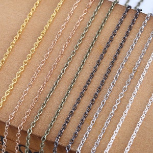 Puede incluir: Surtido de eslabones de cadena en varios colores, incluyendo oro, plata, oro rosa, negro y verde. Las cadenas están dispuestas en líneas paralelas sobre una superficie marrón.
