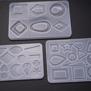 May include: Three clear silicone molds for making jewelry. The molds are rectangular and feature various shapes, including circles, squares, triangles, stars, hearts, and leaves.