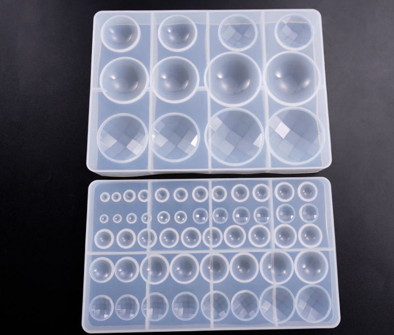 May include: Two clear silicone molds for making resin jewelry. The top mold has six large round cavities and six smaller diamond-shaped cavities. The bottom mold has 36 round cavities of various sizes.
