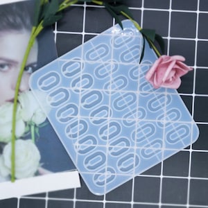 Puede incluir: Un molde de silicona transparente con un patrón repetitivo de formas ovales entrelazadas. El molde está sobre un fondo de cuadrícula blanco y negro.