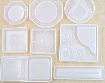 May include: Set of nine white silicone molds for resin casting. The molds are in various shapes, including round, square, and rectangular. Some molds have intricate designs, while others are simple.