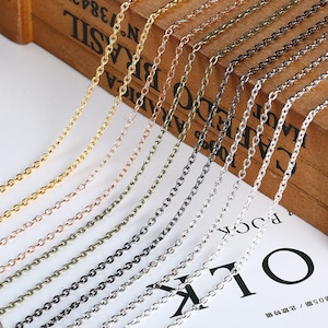 以下が含まれることがあります： ゴールド、銅、シルバーなど、さまざまな金属仕上げの繊細なチェーンネックレスの詰め合わせ。 チェーンは木製の背景に表示され、さまざまな色と質感が示されています。 ジュエリー作りに最適です。