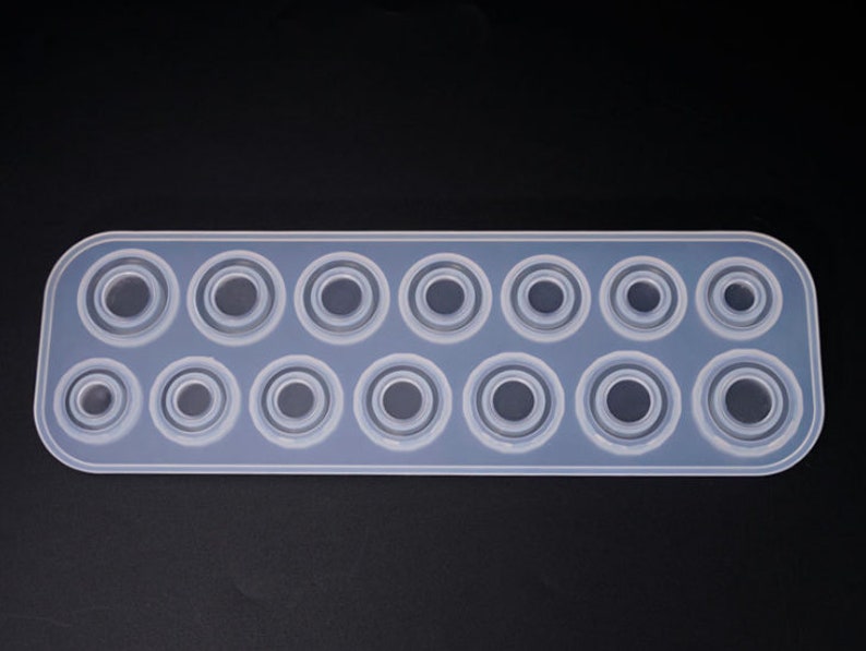 Puede incluir: Un molde de silicona transparente de forma rectangular con una serie de cavidades circulares de varios tama&ntilde;os. El molde est&aacute; dise&ntilde;ado para manualidades, probablemente para resina o materiales similares, y tiene una superficie lisa y antiadherente.