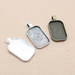 May include: Three silver, bronze, and antique silver pendant trays with a decorative pattern. The trays are rectangular and have a bail for hanging.