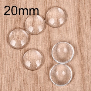 Puede incluir: Seis cabujones de vidrio transparente, cada uno con un diámetro de 20 mm, dispuestos en semicírculo sobre una superficie de madera.