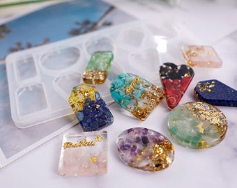 Pode incluir: Um molde de silicone com oito formas diferentes para fazer pingentes de joias de resina. O molde é mostrado com oito pingentes acabados, cada um cheio de pedras de cores diferentes e flocos de ouro.