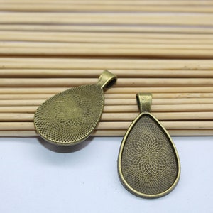 K&ouml;nnte beinhalten: Zwei bronzefarbene Anh&auml;nger-Tabletts in Tropfenform. Die Tabletts haben eine strukturierte Oberfl&auml;che und sind f&uuml;r die Aufnahme eines Cabochons ausgelegt.