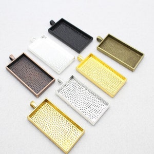 Può includere: Assortimento di sei vassoi rettangolari per ciondoli in diverse finiture, tra cui nero, argento, oro e bronzo. Ogni vassoio ha una superficie testurizzata e un anello per l'appeso.