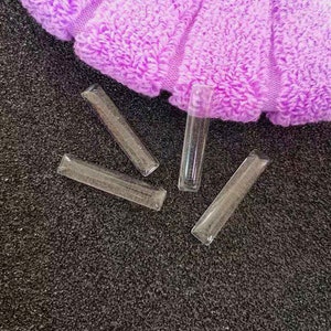 Pode incluir: Quatro pontas de unhas de plástico transparente sobre uma superfície preta texturizada. As pontas são retangulares e têm um acabamento liso.