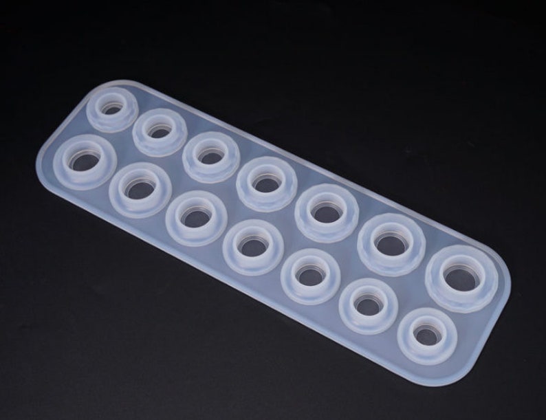 Puede incluir: Un molde de silicona transparente de forma rectangular con m&uacute;ltiples cavidades circulares. El molde est&aacute; dise&ntilde;ado para crear objetos peque&ntilde;os y redondos, con aberturas de diferentes tama&ntilde;os. El fondo es negro liso.