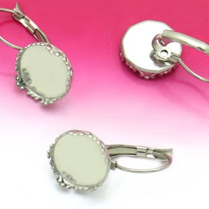 May include: Three silver-toned leverback earring blanks with oval settings. The settings have a decorative, scalloped edge. The earring blanks are shown against a gradient pink and white background.