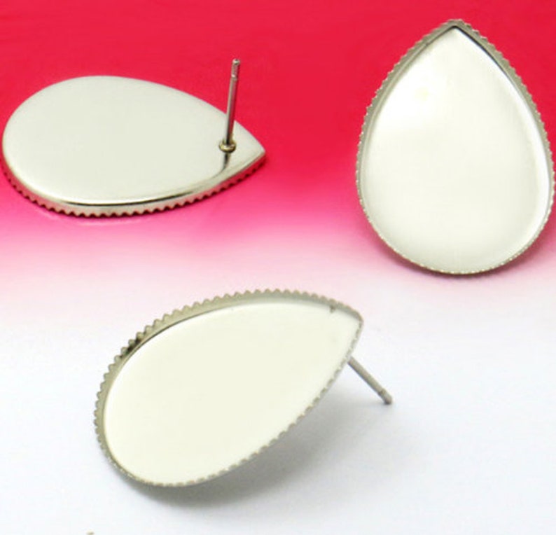 May include: Three silver teardrop-shaped earring blanks with a scalloped edge. The blanks are ready to be filled with resin or other materials.