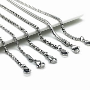 Könnte beinhalten: Sechs silberne Ketten mit Karabinerverschlüssen. Die Ketten sind in verschiedenen Stilen, darunter eine Schlangen-, eine Panzer- und eine Seilkette.