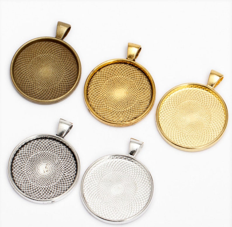 May include: Five round metal pendant trays with a decorative pattern. The trays are in different colors: gold, silver, and bronze. Each tray has a loop at the top for hanging.