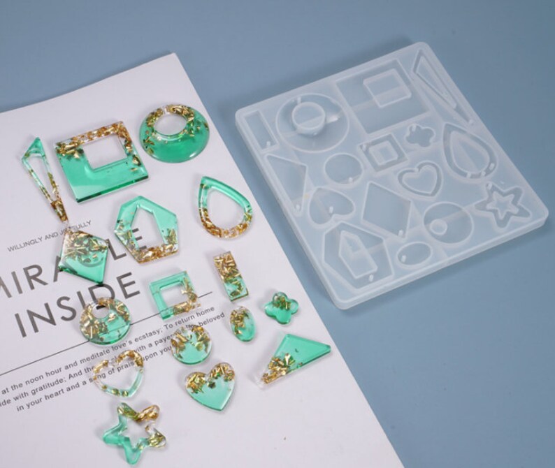May include: A clear silicone mold with various shapes for making earrings. The mold is filled with green and gold resin, showing the finished product.