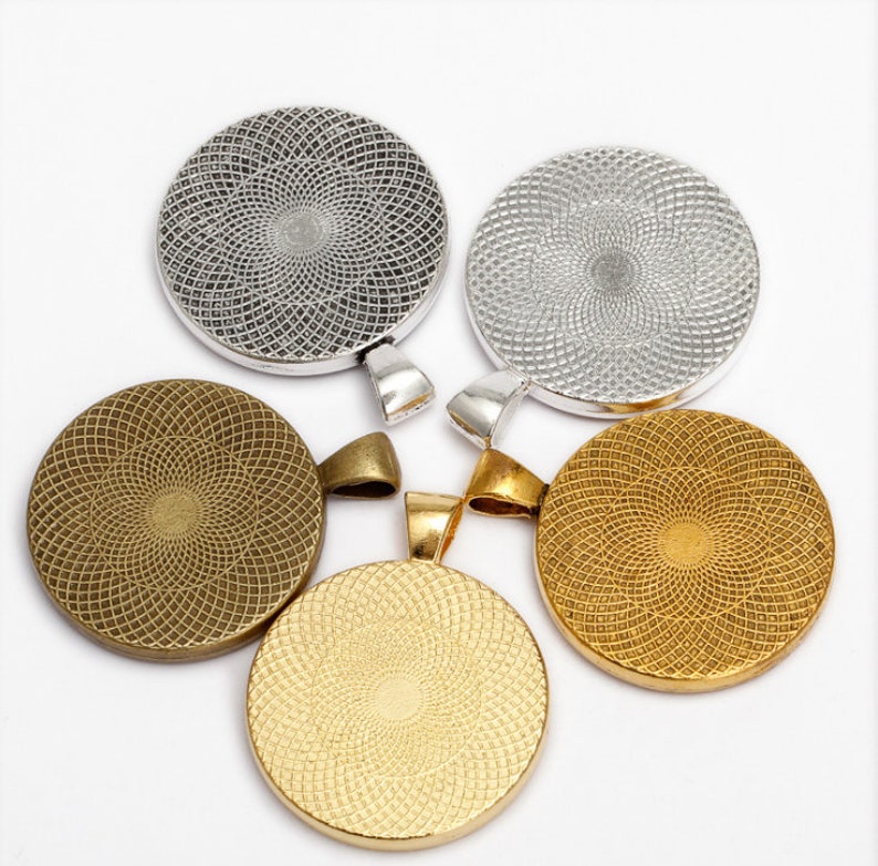 May include: Four round metal pendant bases with a decorative pattern. Two are silver and two are gold.