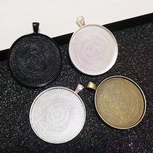 Może przedstawiać: Cztery okrągłe tace do zawieszek z fakturowaną powierzchnią. Tace są w kolorze czarnym, srebrnym i złotym.