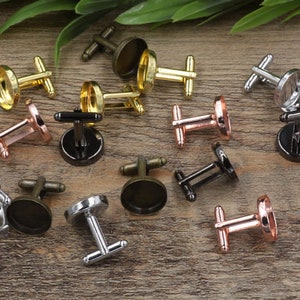 Può includere: Una collezione di 12 gemelli in argento, oro e oro rosa con cabochon rotondi in vetro. I gemelli sono disposti su una superficie in legno.