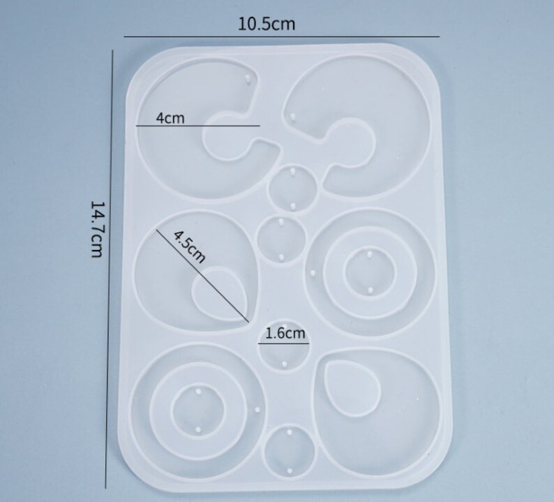 Puede incluir: Un molde de silicona blanco para hacer pendientes. El molde tiene 10 formas diferentes, incluyendo c&iacute;rculos, &oacute;valos y l&aacute;grimas. El molde mide 10,5 cm por 14,7 cm.