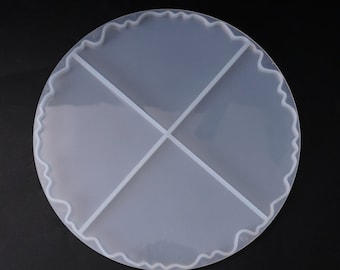May include: A clear, round silicone mold with a wavy edge and cross-shaped dividers. The mold is divided into four sections. The background is black.