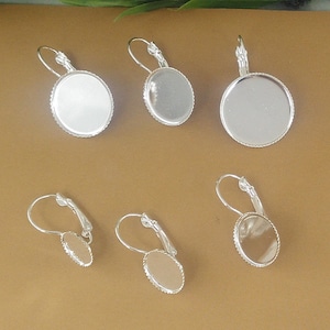 Puede incluir: Cinco bases de pendientes de plata con formas redondas y ovaladas. Las bases son lisas y tienen un acabado brillante.