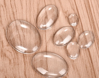 Pode incluir: Um conjunto de seis cabochões ovais de vidro transparente de tamanhos diferentes, dispostos sobre uma superfície de madeira.