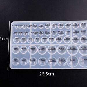 May include: A clear silicone mold with 24 round cavities of different sizes, ranging from 0.5 cm to 3.3 cm in diameter. The mold is 15.4 cm tall and 26.6 cm wide.