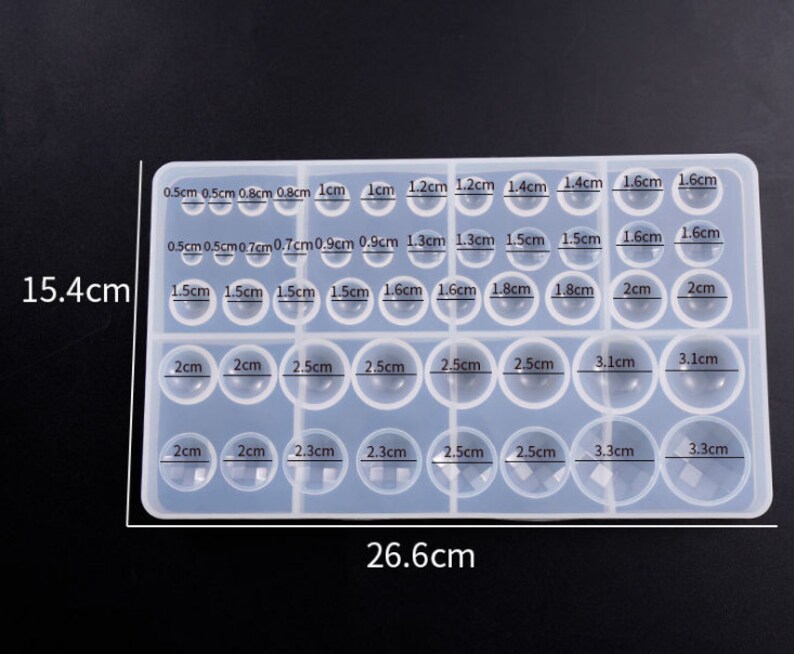 May include: A clear silicone mold with 24 round cavities of different sizes, ranging from 0.5 cm to 3.3 cm in diameter. The mold is 15.4 cm tall and 26.6 cm wide.