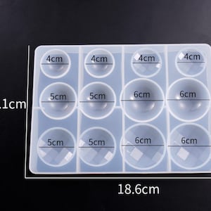May include: A clear silicone mold with 12 round cavities for making resin ornaments. The mold measures 18.6 cm by 26.1 cm and has cavities of 4 cm, 5 cm, and 6 cm in diameter.