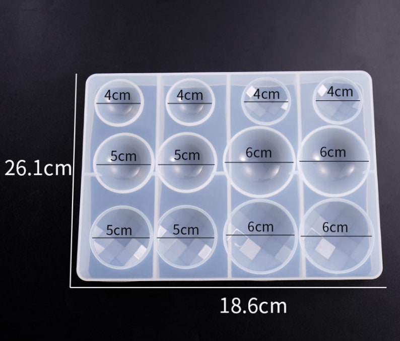 May include: A clear silicone mold with 12 round cavities for making resin ornaments. The mold measures 18.6 cm by 26.1 cm and has cavities of 4 cm, 5 cm, and 6 cm in diameter.