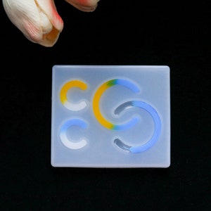 May include: A clear silicone mold with three different shapes of curved lines. The lines are in shades of blue, yellow, and white.