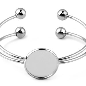 May include: Silver bangle bracelet with a round, blank, silver charm in the center. The bracelet has two silver balls on each side.