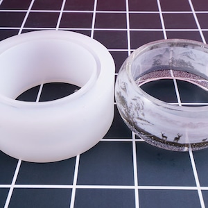 Pode incluir: Um molde de silicone branco e um bracelete de resina transparente com uma cena de inverno e uma silhueta de veado no interior.