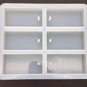 May include: A white silicone mould with six rectangular cavities. The mould is designed for making small rectangular objects, such as soap bars or resin crafts.