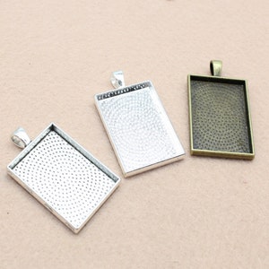 Puede incluir: Tres bandejas rectangulares de plata para colgantes con una superficie texturizada. Las bandejas tienen un bucle en la parte superior para sujetar una cadena o un cordón.