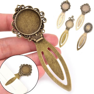 Puede incluir: Un conjunto de cinco colgantes de marcapáginas de metal dorado antiguo con un cabujón redondo de vidrio en el centro. Los marcapáginas presentan una variedad de diseños, que incluyen una corona, un patrón floral y una forma ovalada simple.