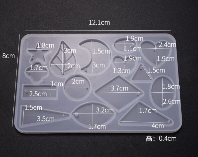 May include: A clear silicone mold with 14 different shapes for resin casting. The shapes include a star, leaf, crescent moon, circle, oval, heart, triangle, rectangle, and more. The mold measures 12.1 cm by 8 cm and is 0.4 cm high.