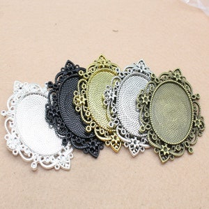 May include: Five ornate metal frames with oval openings, each with a different finish: silver, black, gold, silver, and bronze. The frames are intricately detailed with floral patterns.